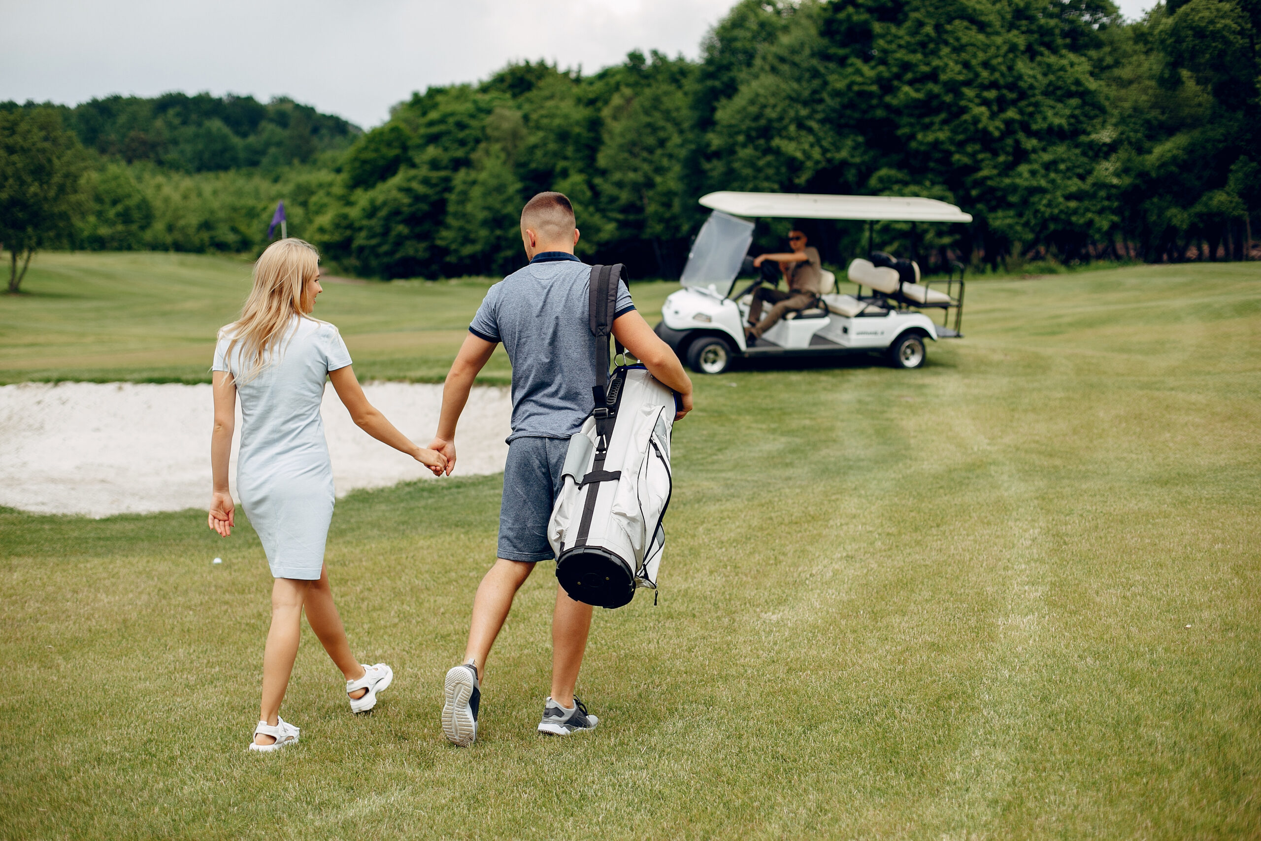 Couple in a golf course. Blonde in a sport clothes. Pair playing golf